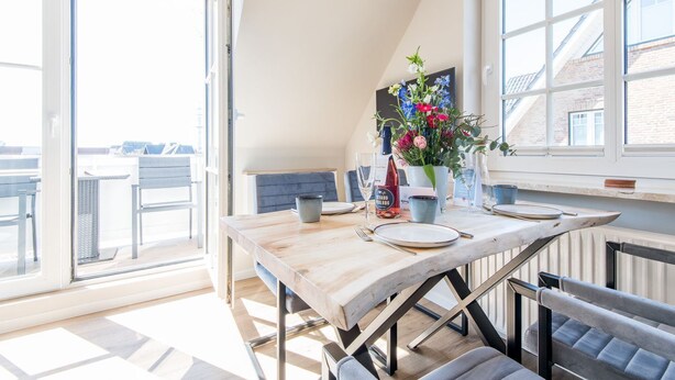 Een eethoek met een houten tafel, stoelen en een vaas met bloemen.