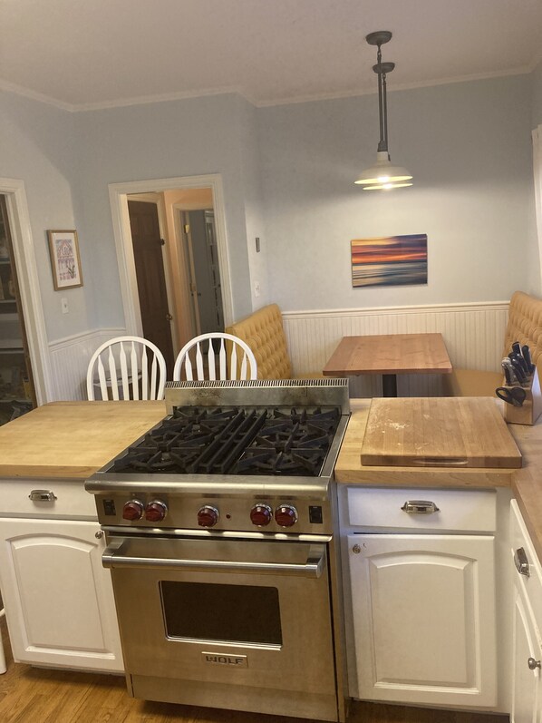 A kitchen with a Wolf stove, white cabinetry, a wooden dining table, and a bench.