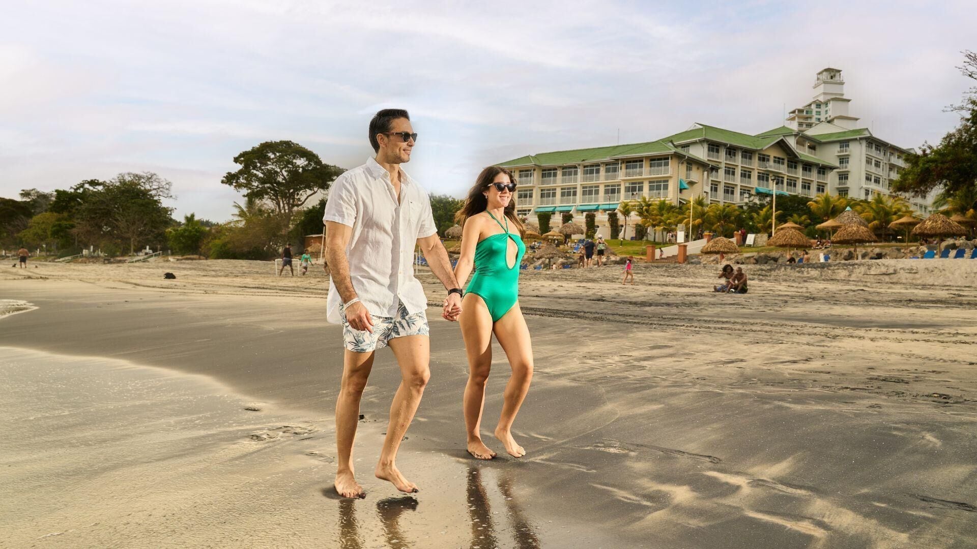 A couple walking on a beach with a large building in the background.