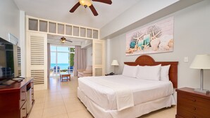 A hotel room with a bed, a desk, a chair, a TV, a ceiling fan, a painting, and a view of the ocean. - Gran Evenia Bijao - All Inclusive (Rio Hato)