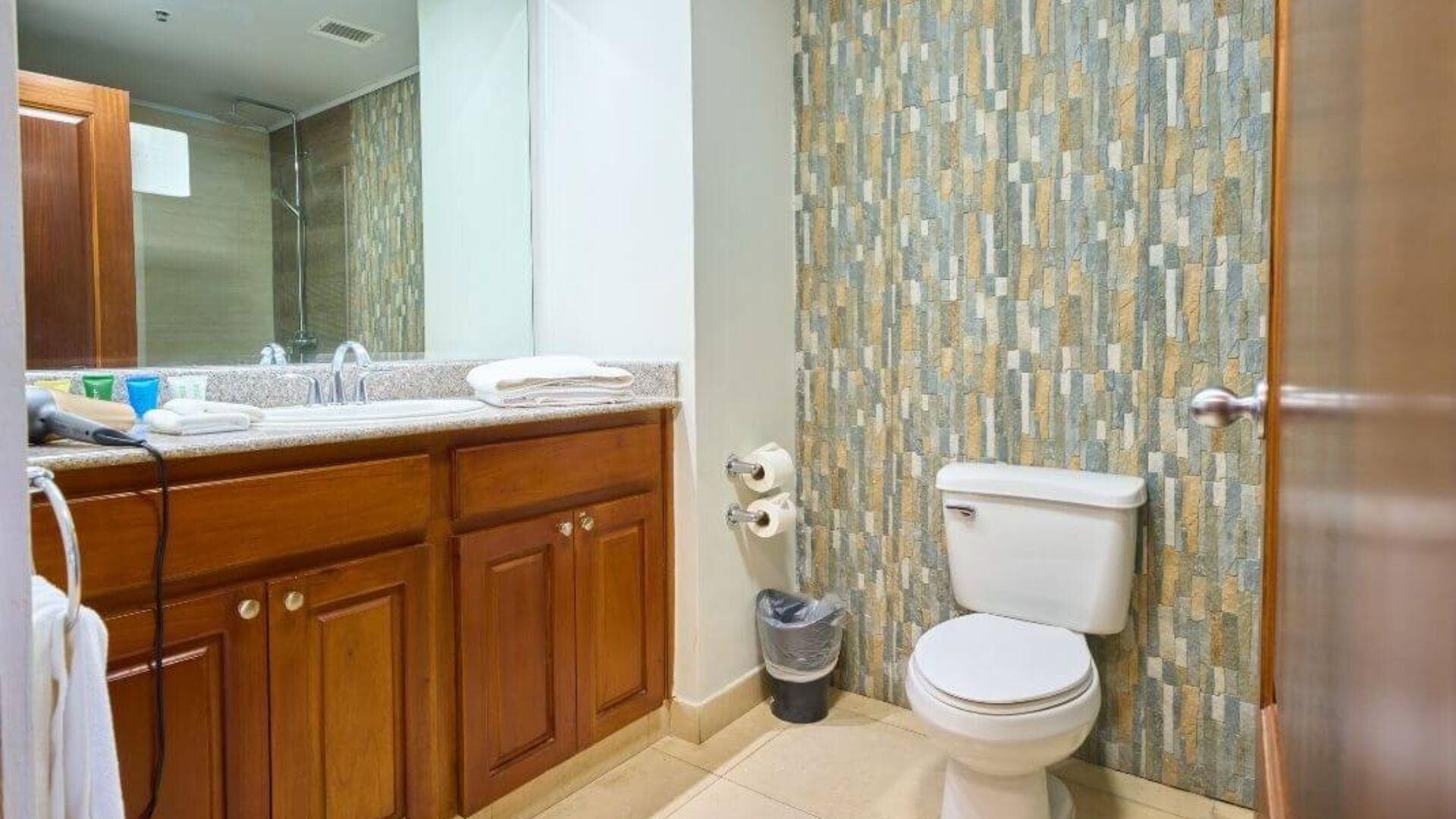 Un baño con tocador de madera, lavamanos, inodoro y cubo de basura.