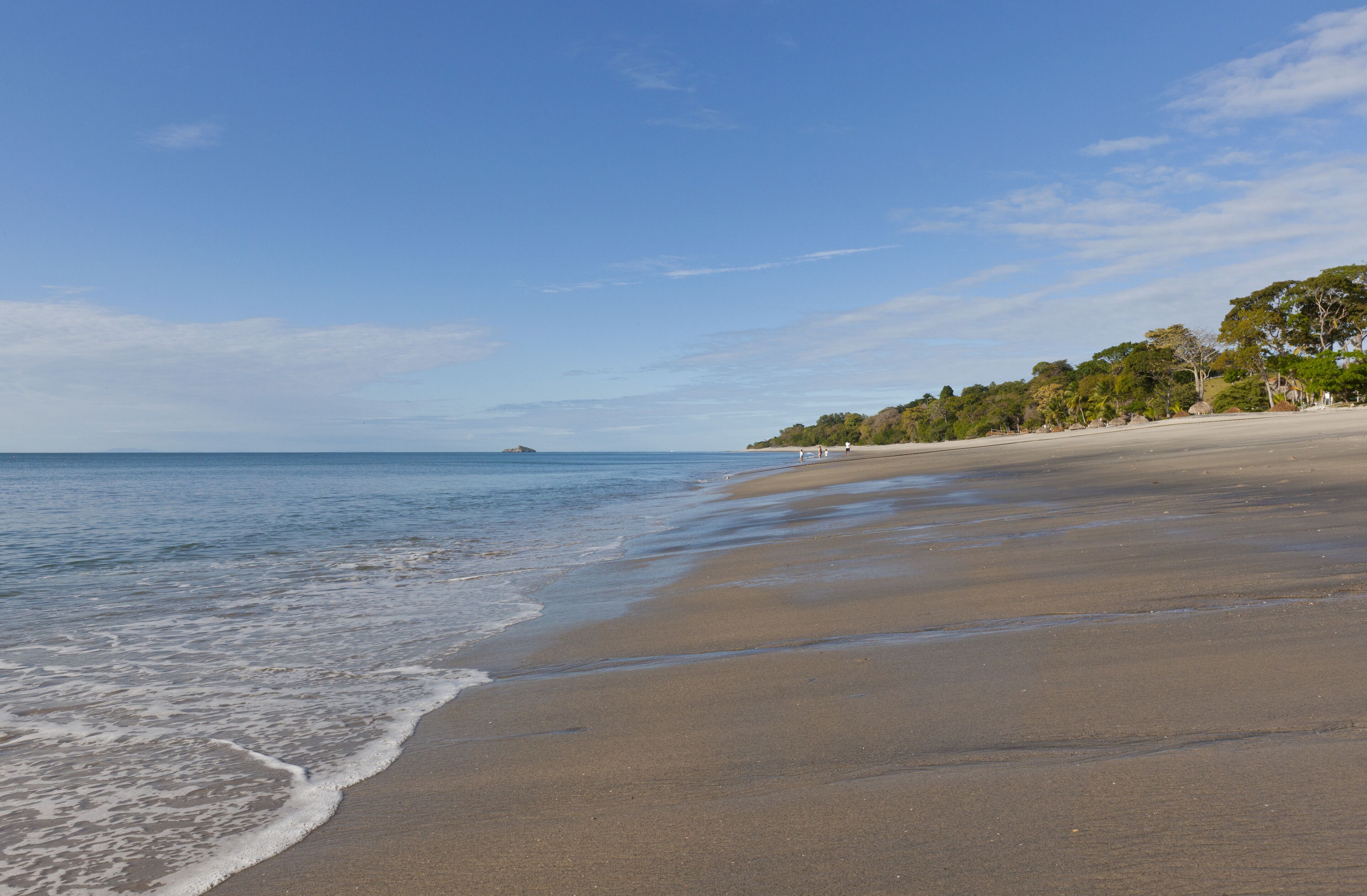 A wide sandy beach with gentle waves, a clear sky, and a distant island.