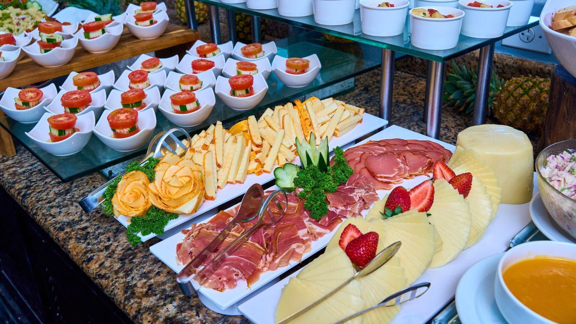 Ein Buffet mit verschiedenen Speisen, darunter Aufschnitt, Käse, Obst und Gemüse.