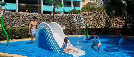 A water park with a large slide, a pool, and a stone wall.