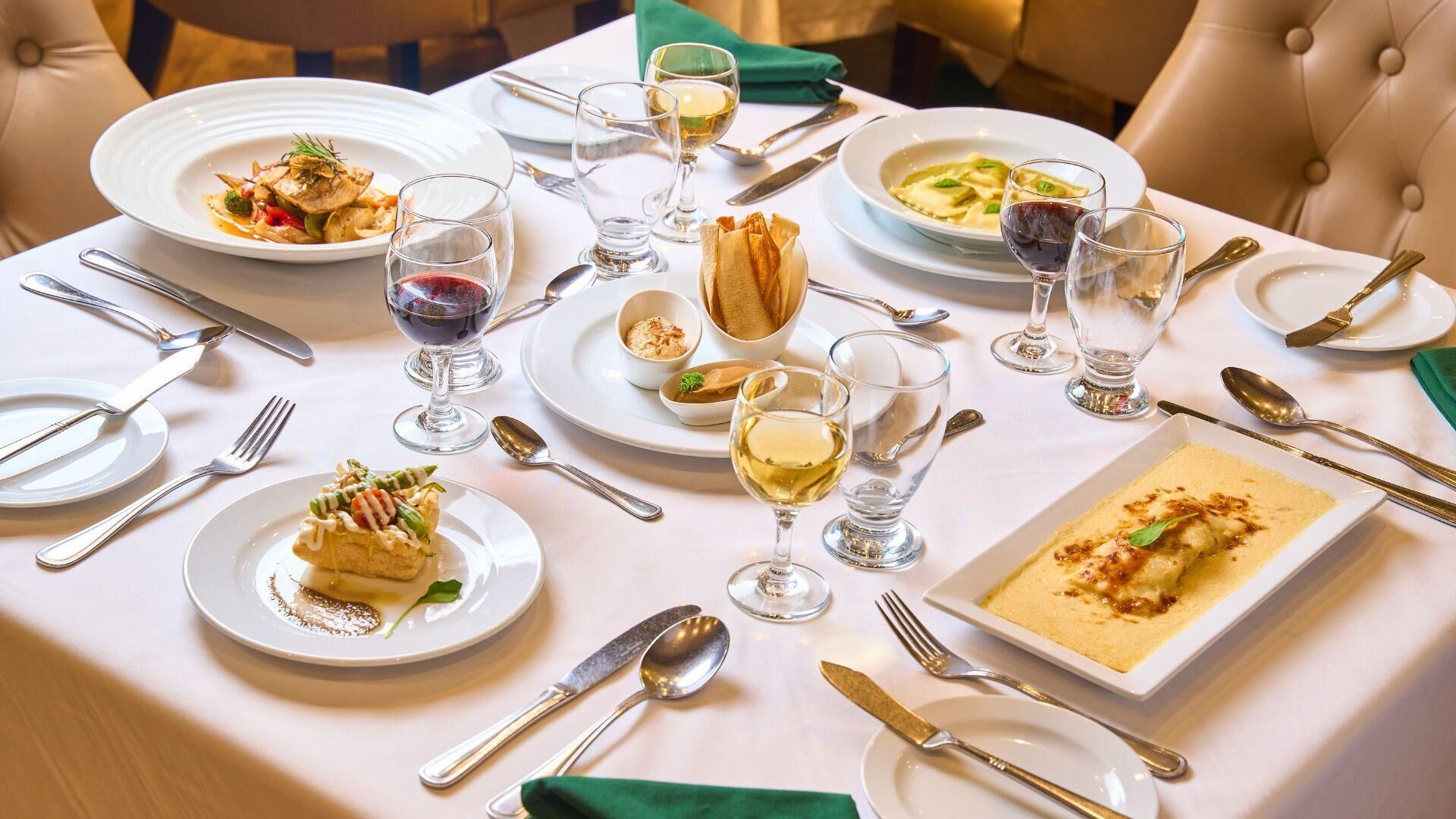Una mesa de comedor dispuesta con platos de comida, copas de vino y cubiertos.