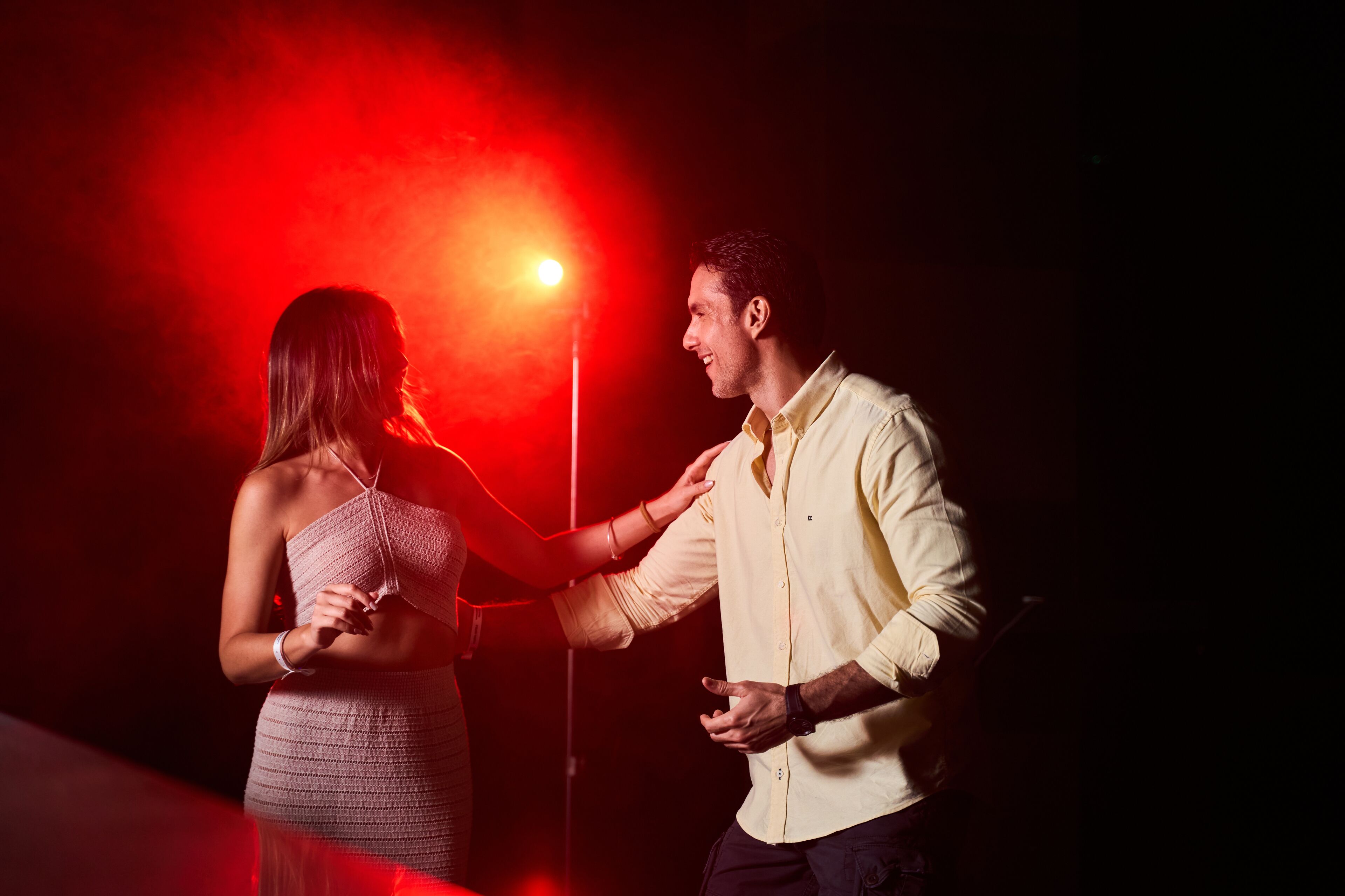 A couple dancing in a dimly lit room with a red light in the background.