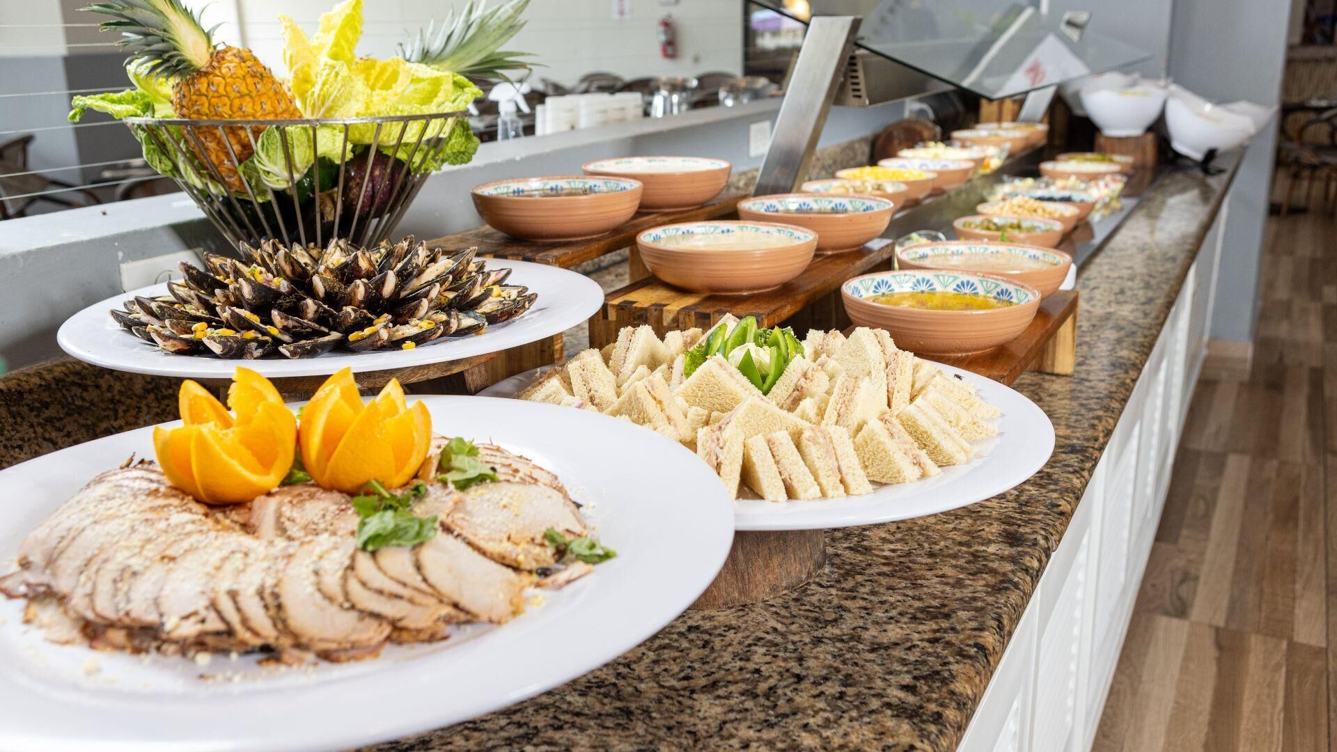 Un bufé con diversos platos, incluyendo carne en rodajas, sándwiches y mariscos.