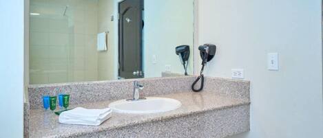 Un baño con encimera de granito, un lavabo, un espejo y dos secadores de pelo fijados a la pared.