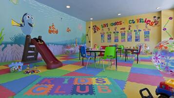 Zona de juegos infantiles con un tobogán, alfombras de juego coloridas y carteles educativos en las paredes.