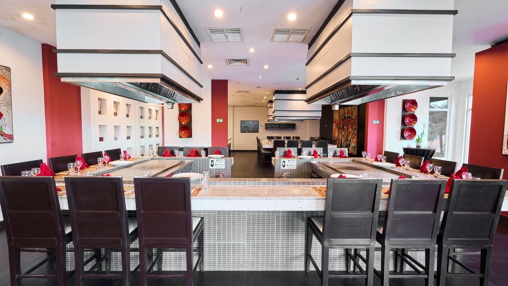 A modern dining area with long tables and black chairs, featuring a central island and a large window on one side.