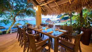 An outdoor dining area with a view of the ocean, thatched roof, wicker furniture, and potted plants. - Gran Evenia Bijao - All Inclusive (Rio Hato)