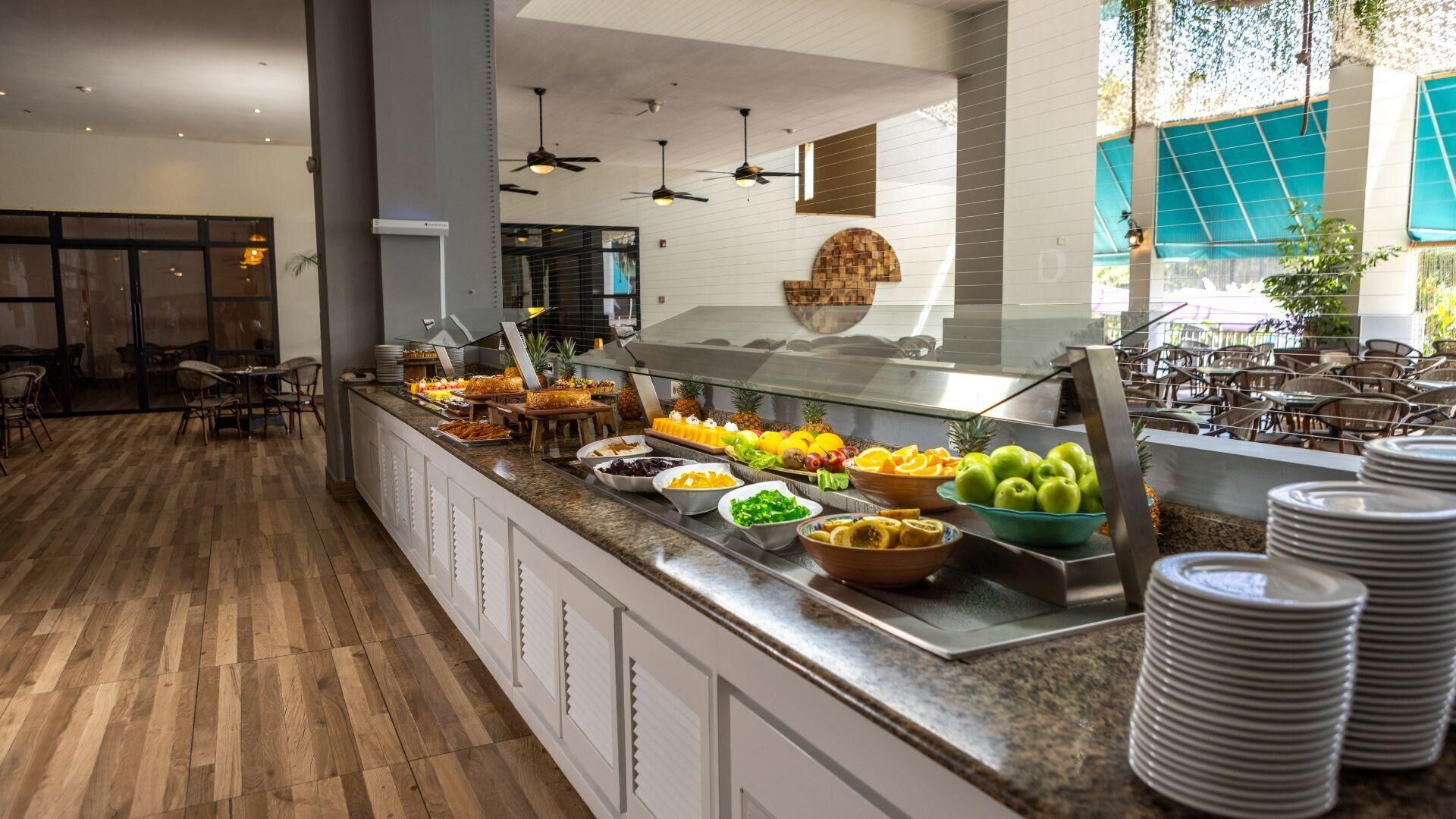 Un espace buffet proposant une variété de plats, un coin repas avec des tables et des chaises, et une vue sur l’extérieur grâce à de grandes fenêtres.