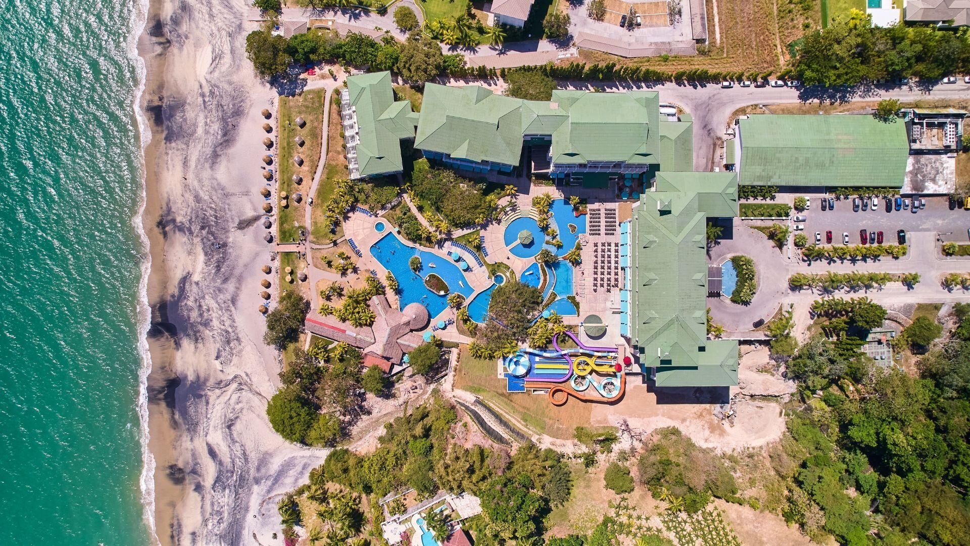 An aerial view of a resort with multiple swimming pools, a beach, and a parking area.