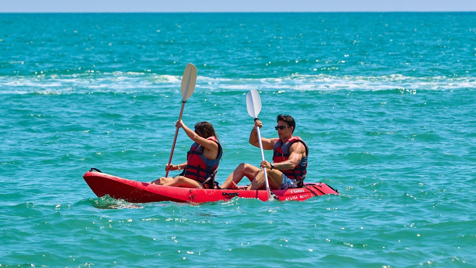 Dos personas remando en un canoa roja sobre aguas turquesas.