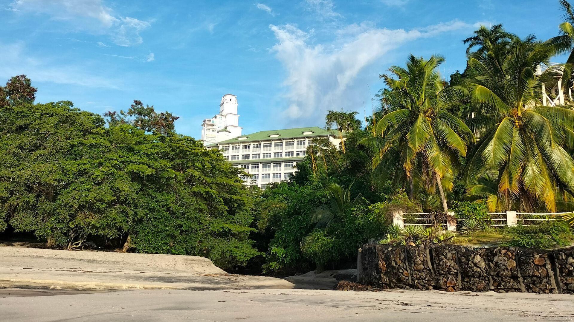 A hotel with a white facade, multiple floors, and a green roof.