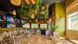 A bar area with multiple screens, wicker furniture, and hanging plants. - Gran Evenia Bijao - All Inclusive (Rio Hato)
