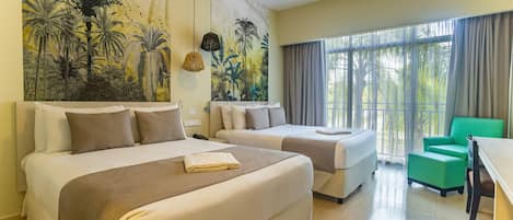 Habitación de hotel con dos camas, una silla verde, una mesa y un gran mural tropical en la pared.