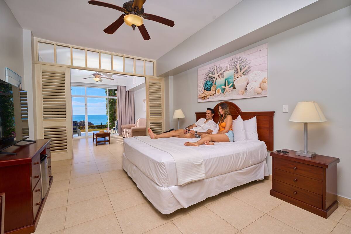 A bedroom with a bed, bedside tables, a ceiling fan, and a view through an open door.