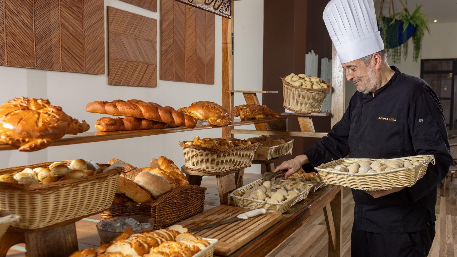 Een bakkerijvitrine met diverse broden en gebak, een kok in uniform, en brodenmanden op een houten toonbank.