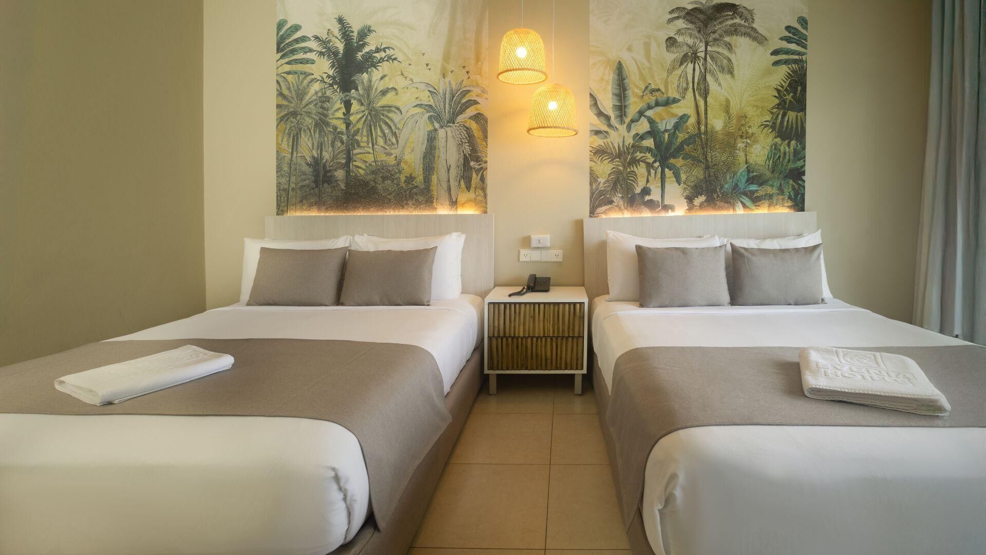 Habitación de hotel con dos camas, una mesita de noche con teléfono y un tapiz de follaje tropical en la pared.