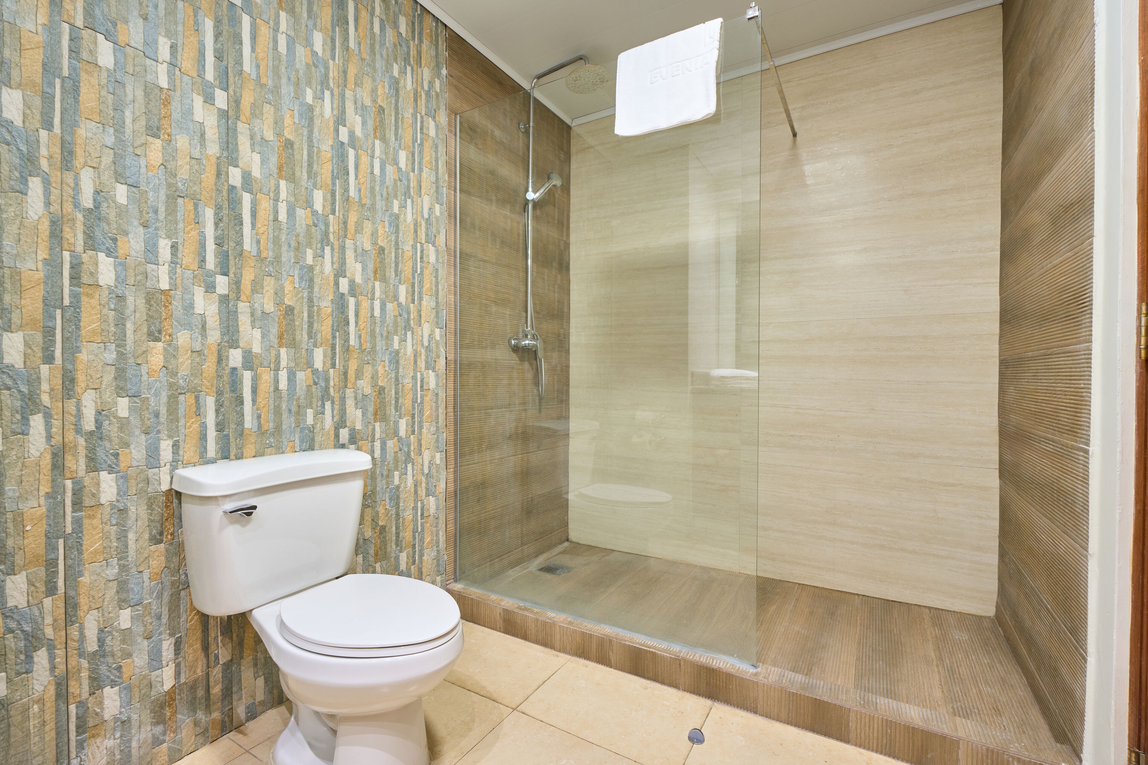 A bathroom with a toilet, a shower with a glass door, and a tiled wall.