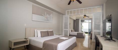 A modern hotel room with a bed, bedside table, ceiling fan, and a view through a door.