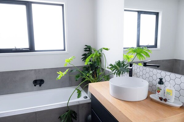 A modern bathroom with a bathtub, a round sink, and two windows. - Ocean views, spacious & private, hot hub (Lower Snug)
