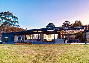 A modern house with a covered patio area, large windows, and a well-maintained lawn. - Ocean views, spacious & private, hot hub (Lower Snug)