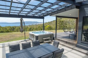A covered outdoor area with a hot tub, seating, and a view of the landscape. - Ocean views, spacious & private, hot hub (Lower Snug)