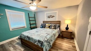 A bedroom with a bed, a ceiling fan, a nightstand, a lamp, and a window with blinds.