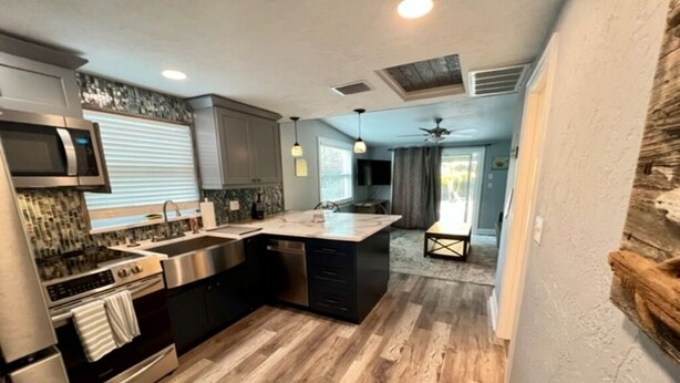 A modern kitchen with a central island, stainless steel appliances, and a wooden floor.