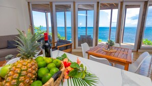 Een eethoek met een tafel gedekt voor twee personen, een houten tafel, en uitzicht op de oceaan door grote glazen schuifdeuren.