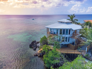 A coastal house with a deck overlooking the sea, surrounded by lush greenery and a clear view of the ocean. - Wow!  Views and more, fantastic 2 bedroom  in West End - Villa Agua (Roatan)