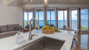 Een moderne keuken met een groot eiland, een roestvrijstalen spoelbak en uitzicht op zee.