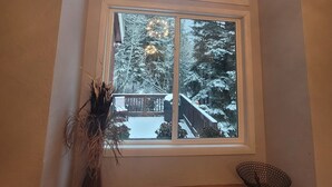 Una stanza con un'ampia finestra vista su un paesaggio innevato, una panca di legno e un tavolino con un oggetto decorativo.