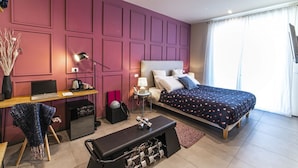 Quarto moderno com uma cama grande, uma escrivaninha com um laptop, um banco e uma pequena mesa com um abajur.