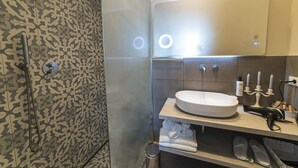 A bathroom with a patterned tile wall, a white sink with a mirror above it, and a shower area with a handheld showerhead. - Double/twin room with bathroom and king size bed near Pescara airport (Pescara)