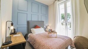 A bedroom with a bed, a desk with a lamp, a chair, and a window with curtains.