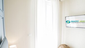 A hotel room with a bed, a lamp, a wall-mounted TV, and a door.