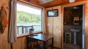 Eine Holzhütte mit Esstisch, Stühlen, einer kleinen Küche mit Spüle und Seeblick durch ein Fenster.