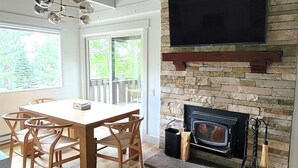 Een eethoek met een houten tafel en stoelen, een stenen openhaard en een wandgemonteerde televisie.