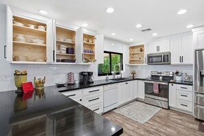 A modern kitchen with white cabinetry, a black countertop, stainless steel appliances, and a window providing natural light.