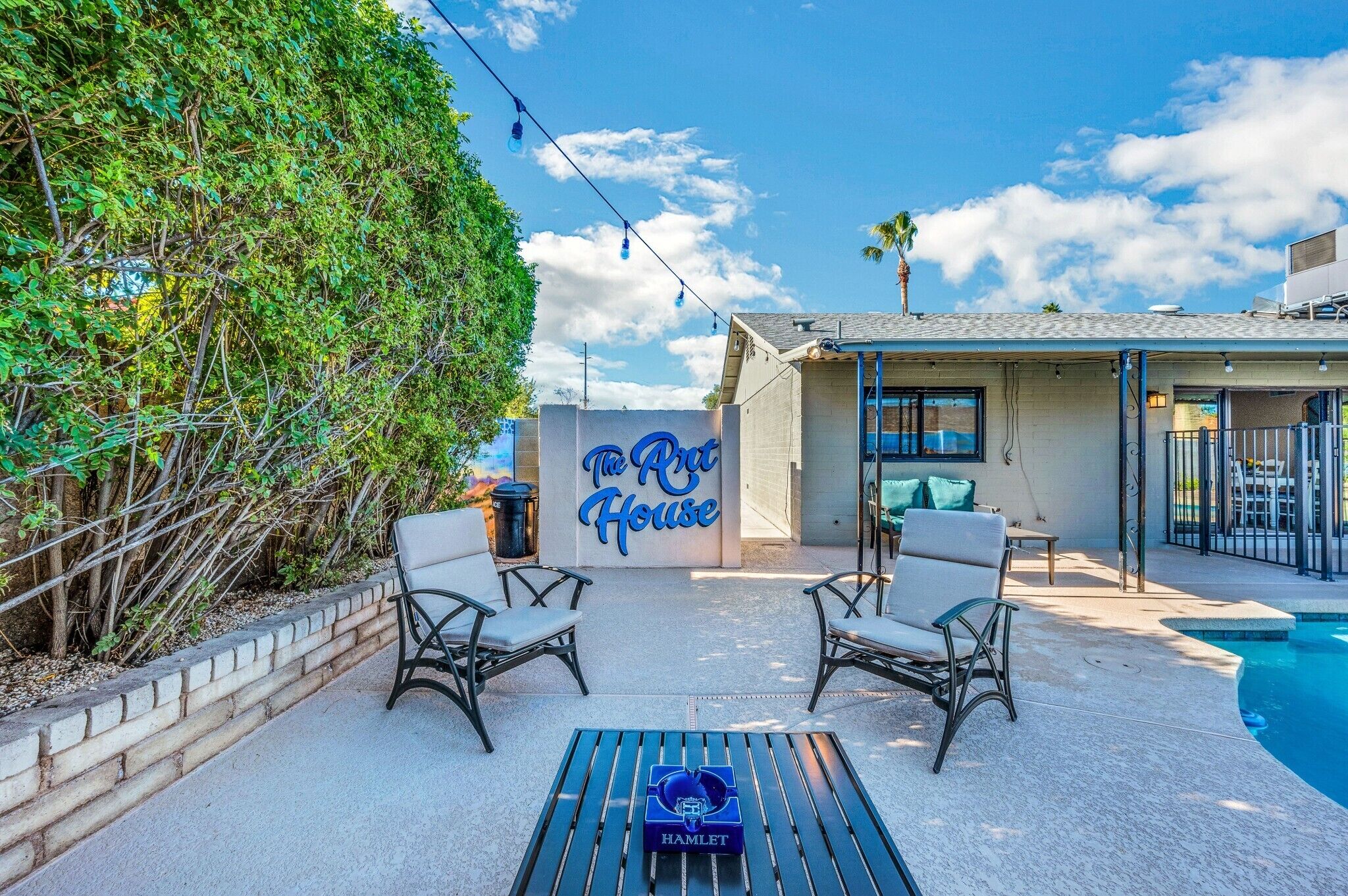 A backyard with a pool, two chairs, a table, and a sign for 'The Art House'.