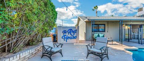 A backyard with a pool, two chairs, a table, and a sign for 'The Art House'.