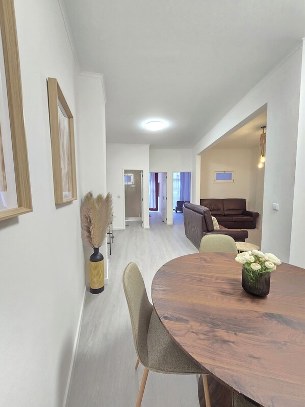 A modern living room with a wooden dining table, grey upholstered chairs, a brown sofa, and a vase with white flowers. - Apt Porto Ribeira Rio Douro - 6 Guests (Porto)