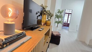 A modern living room with a wooden entertainment unit, a flat-screen TV, a decorative light, and a potted plant. - Apt Porto Ribeira Rio Douro - 6 Guests  (Porto)
