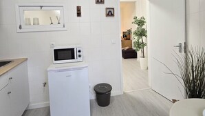 A modern kitchen with white appliances, a microwave, and a small trash bin. There are framed pictures on the wall and a doorway leading to another room. - Apt Porto Ribeira Rio Douro - 6 Guests  (Porto)