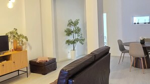 A modern living room with a black leather sofa, a wooden TV stand, a dining area with a round table and chairs, and a potted plant. - Apt Porto Ribeira Rio Douro - 6 Guests  (Porto)