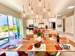 A modern kitchen with white cabinets, a central island, and a dining area set for six with a wooden table, red napkins, and a vase of flowers.