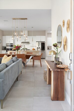 A modern kitchen with white cabinets, a dining area with a wooden table and chairs, and a gray sofa with yellow cushions.